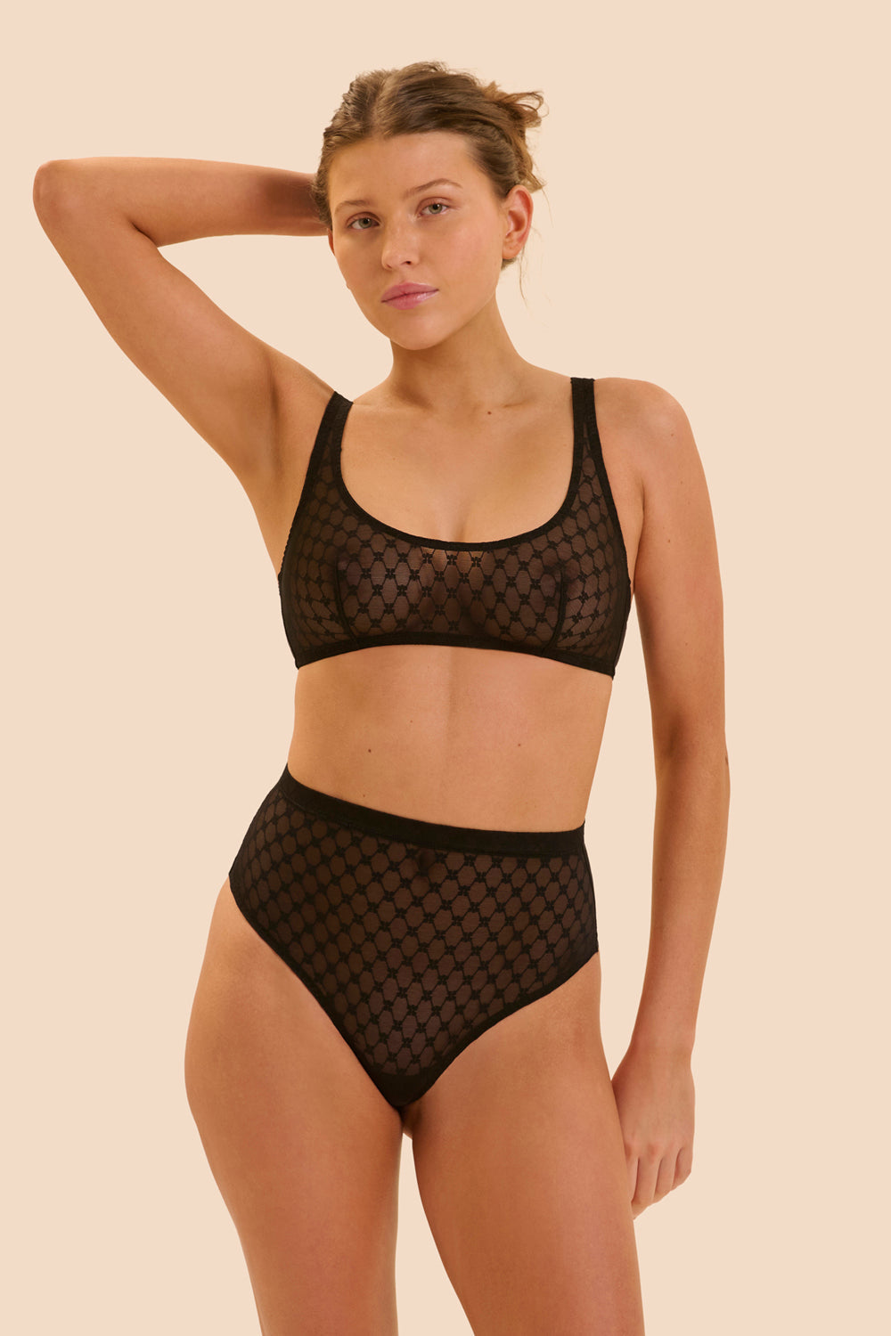 Woman wearing a black mesh lingerie set on a beige background