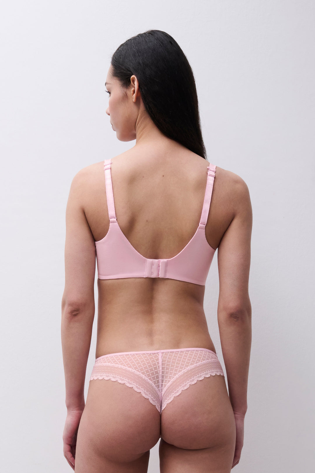 Woman wearing a pink bra and panties set against a plain background