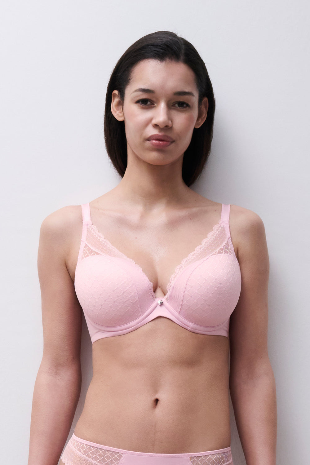 Woman wearing a pink bra and underwear set against a plain background