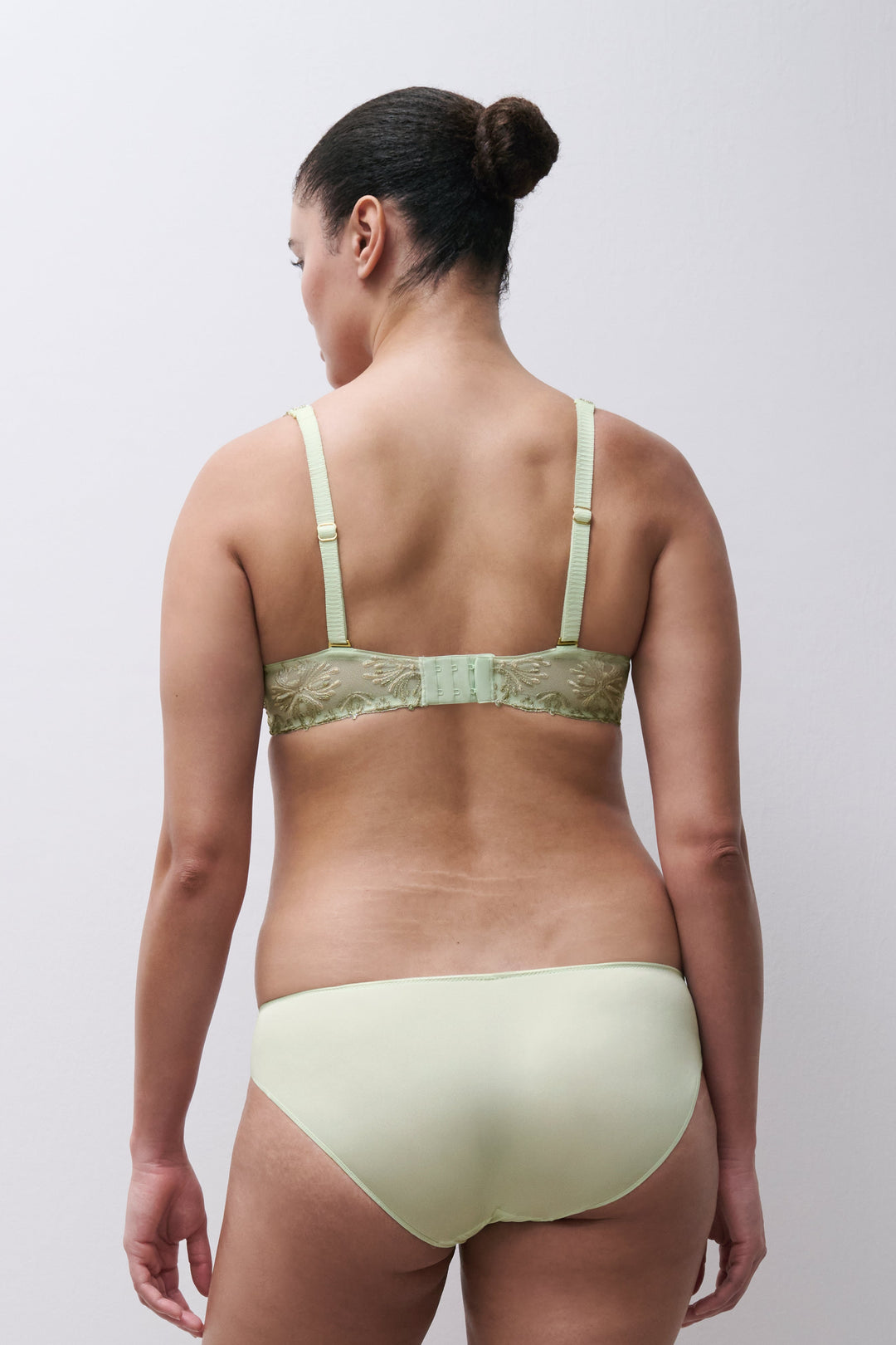 Woman wearing a light green bra and panties set against a plain background