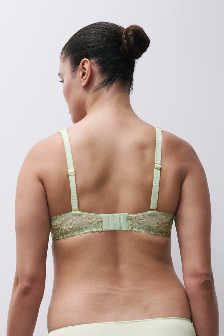 Woman wearing a light green bra with floral lace details on a plain background