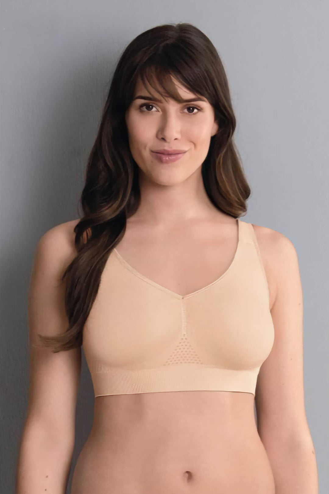 Woman wearing a beige wireless bra against a gray background