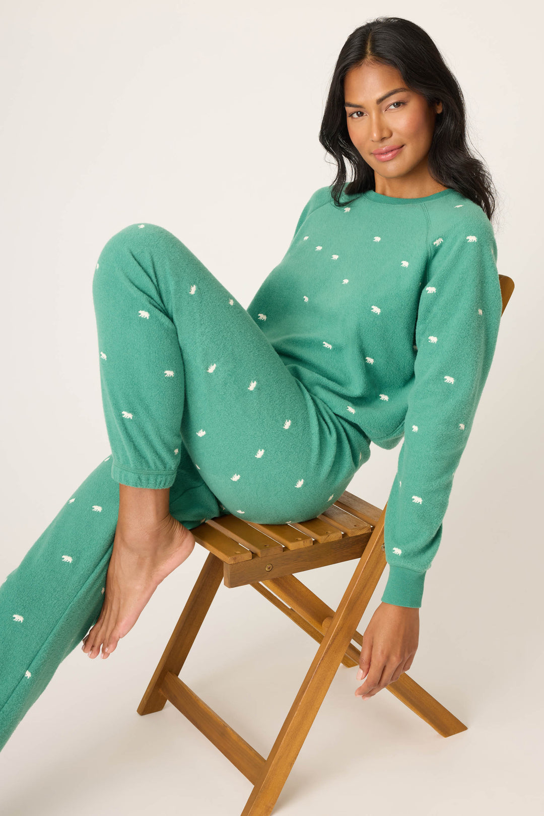 Woman wearing a green bear print outfit sitting on a wooden stool against a white background