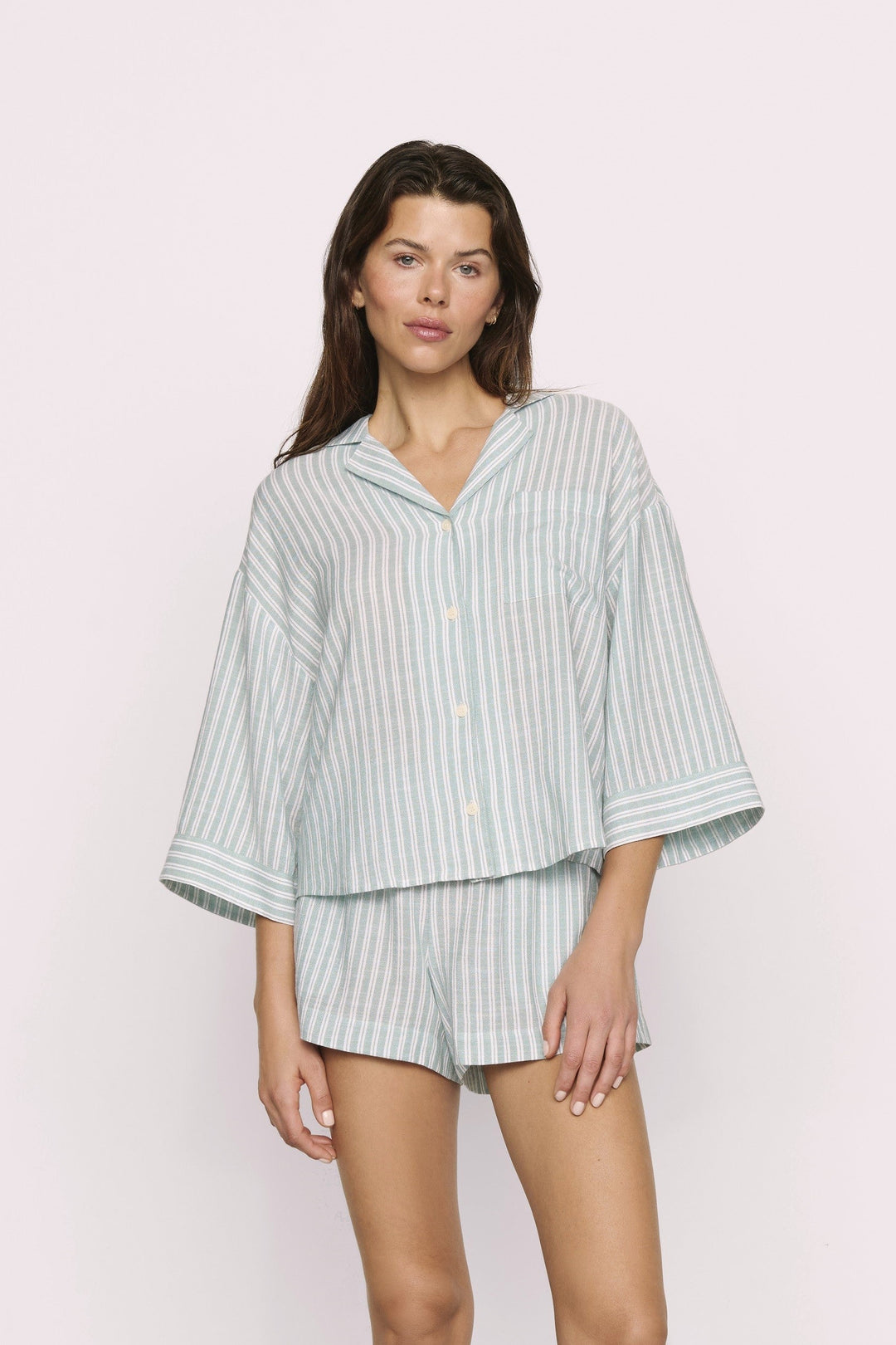 Woman wearing a light green and white striped pajama set against a plain background