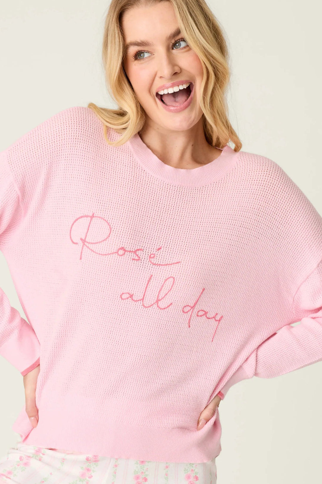 Woman wearing a pink sweatshirt with 'Rose all day' text and matching shorts on a white background