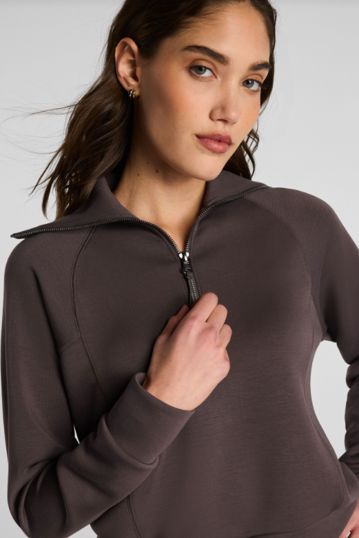 Woman wearing a brown zip-up sweatshirt against a plain background