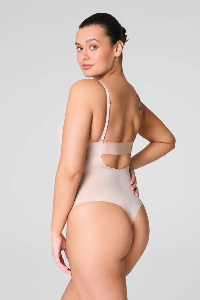 Woman wearing a beige bodysuit against a light gray background