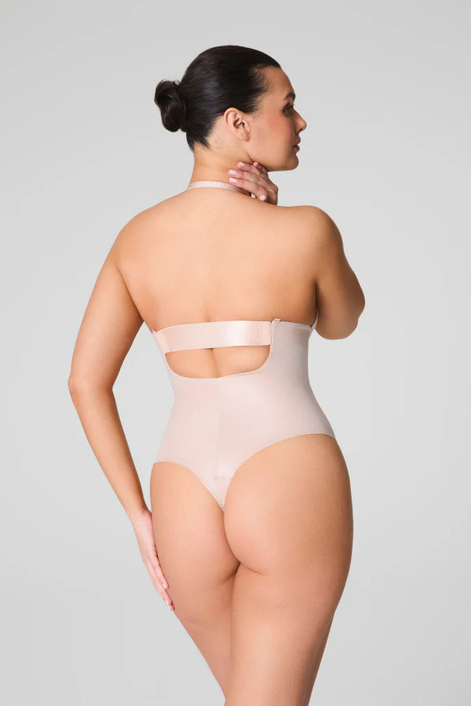 Woman wearing a beige bodysuit against a gray background