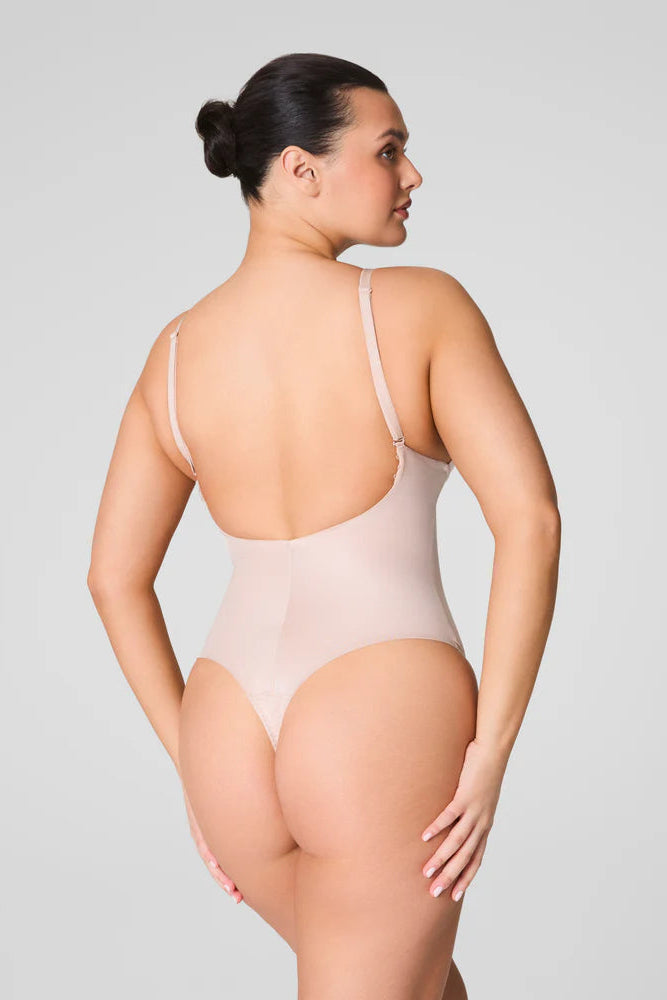 Woman wearing a beige bodysuit against a plain background