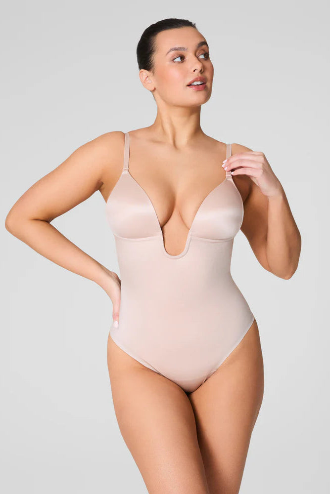 Woman wearing a beige bodysuit against a plain background