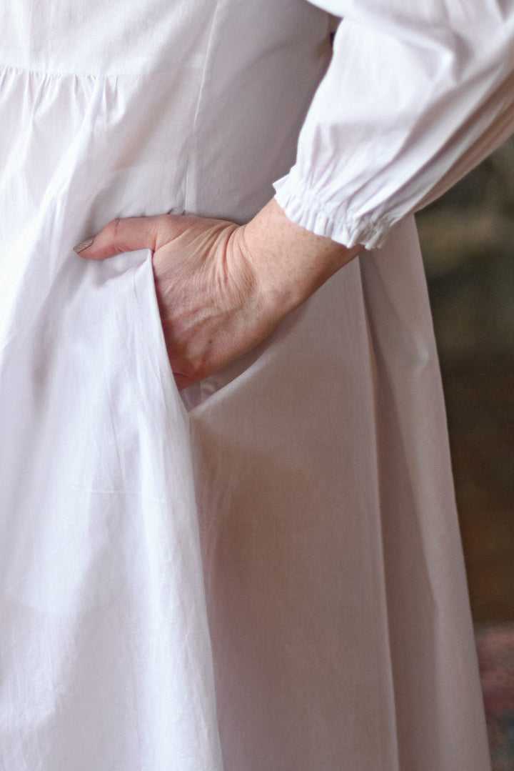 Close-up of a person wearing a white nightdress with long sleeves and a plain background.