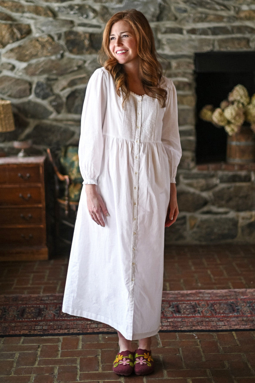 Woman in a white nightdress standing in front of a stone fireplace.