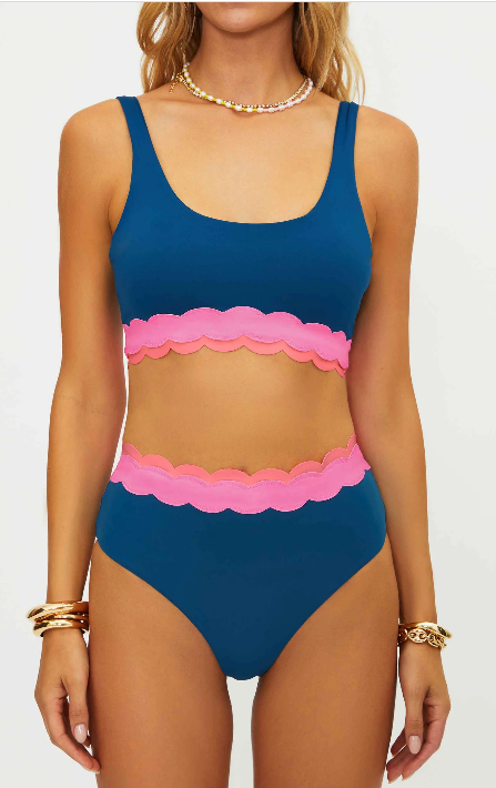 Woman wearing a blue and pink bikini with scalloped edges on a white background