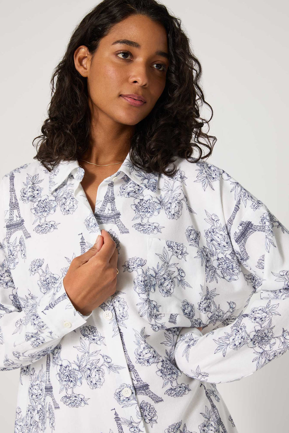 Woman wearing a white shirt with blue floral patterns on a plain background