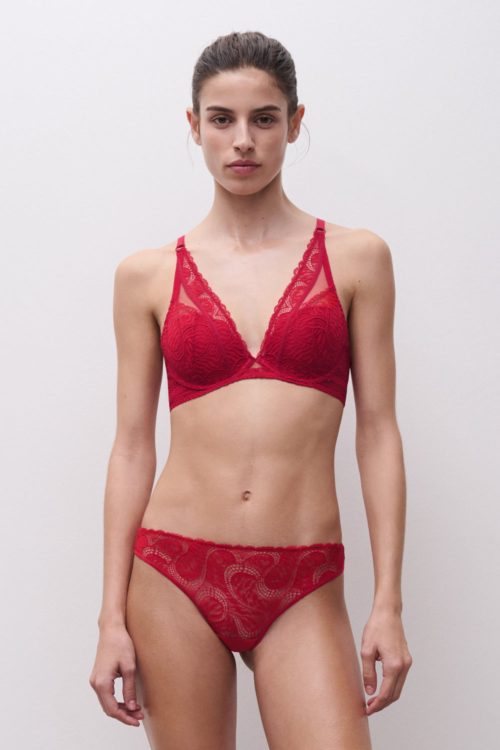 Model wearing a red lace lingerie set against a plain background