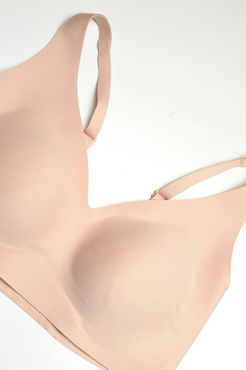 A close-up of a seamless, light peach-beige wireless bra cup and strap, laid flat on a clean white background.