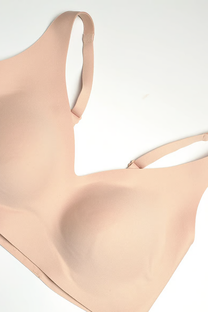 A close-up of a seamless, light peach-beige wireless bra cup and strap, laid flat on a clean white background.