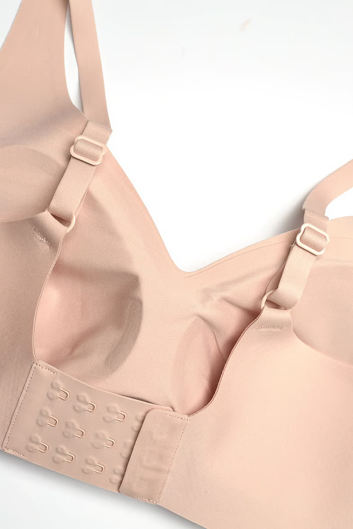 Close-up of a light beige wireless bra with adjustable straps and a hook-and-eye back closure, photographed on a plain white background.