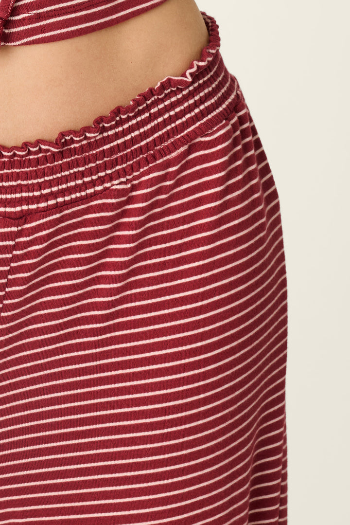 Close-up of a person wearing red and white horizontally striped knit bottoms with a smocked elastic waistband, against a plain light background.