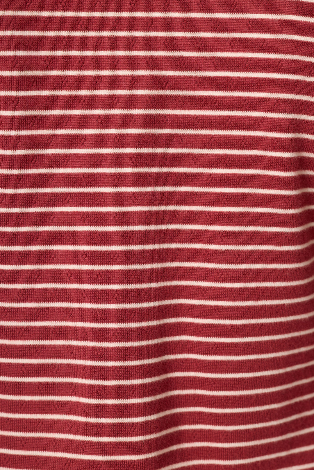 A close-up of a red knit fabric with thin, evenly spaced horizontal white stripes.