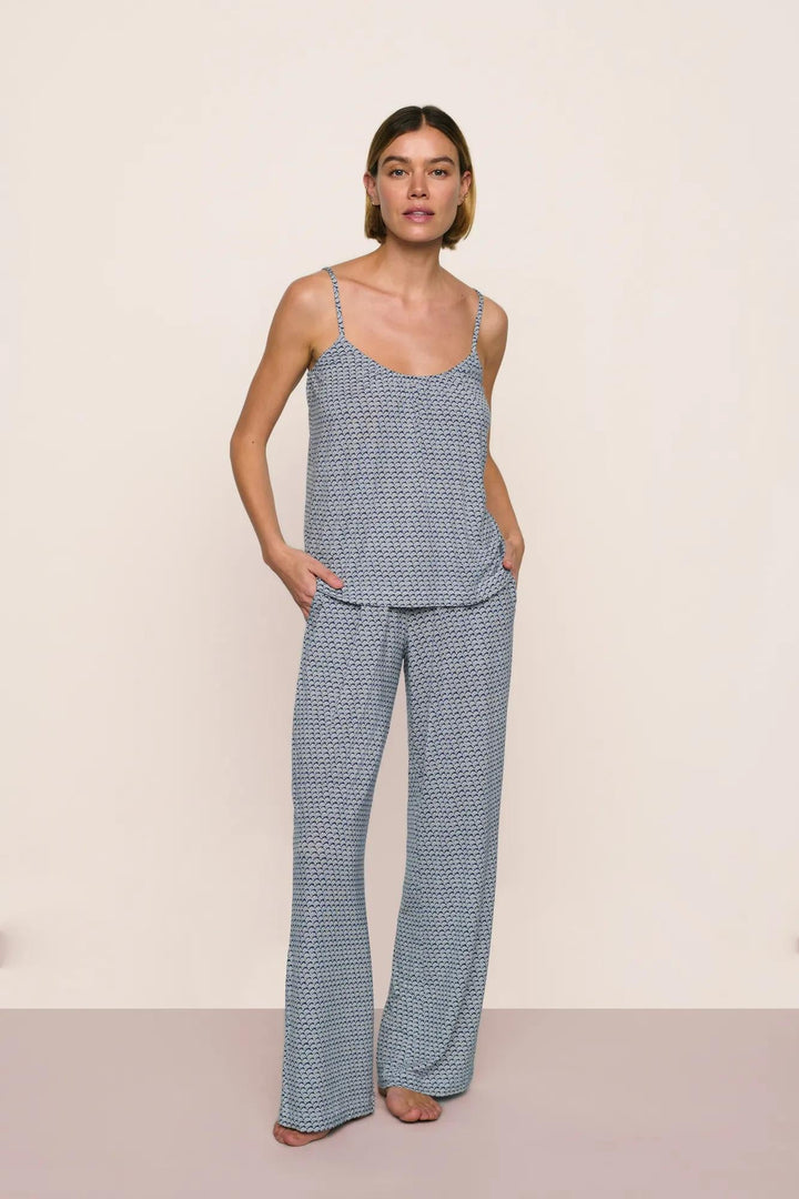 Woman wearing a blue seashell patterned camisole and pant pajama set against a beige background
