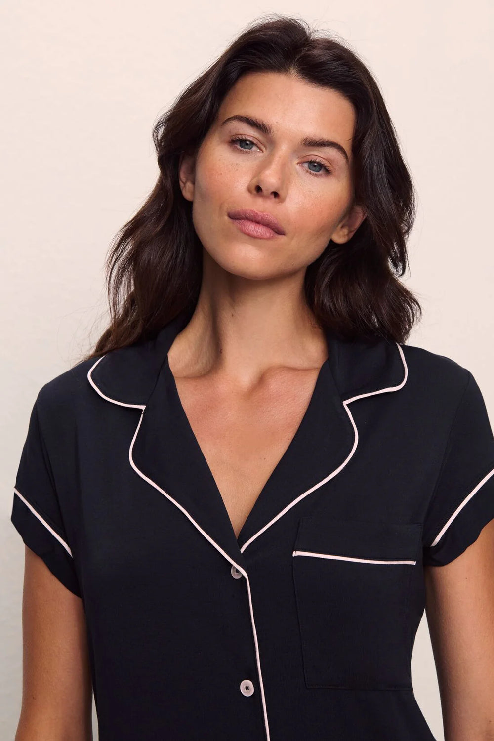 Woman wearing a black pajama top with white piping against a plain background
