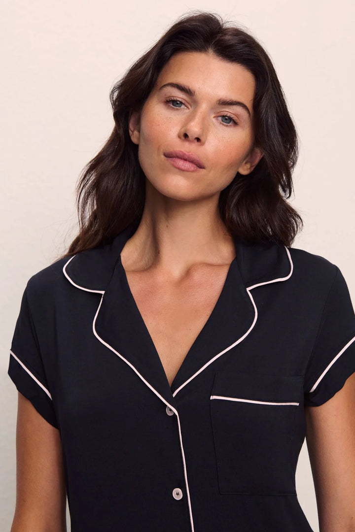 Woman wearing a black pajama top with white piping against a plain background