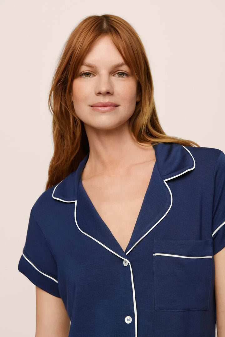 Woman wearing a navy blue pajama top with white trim on a beige background