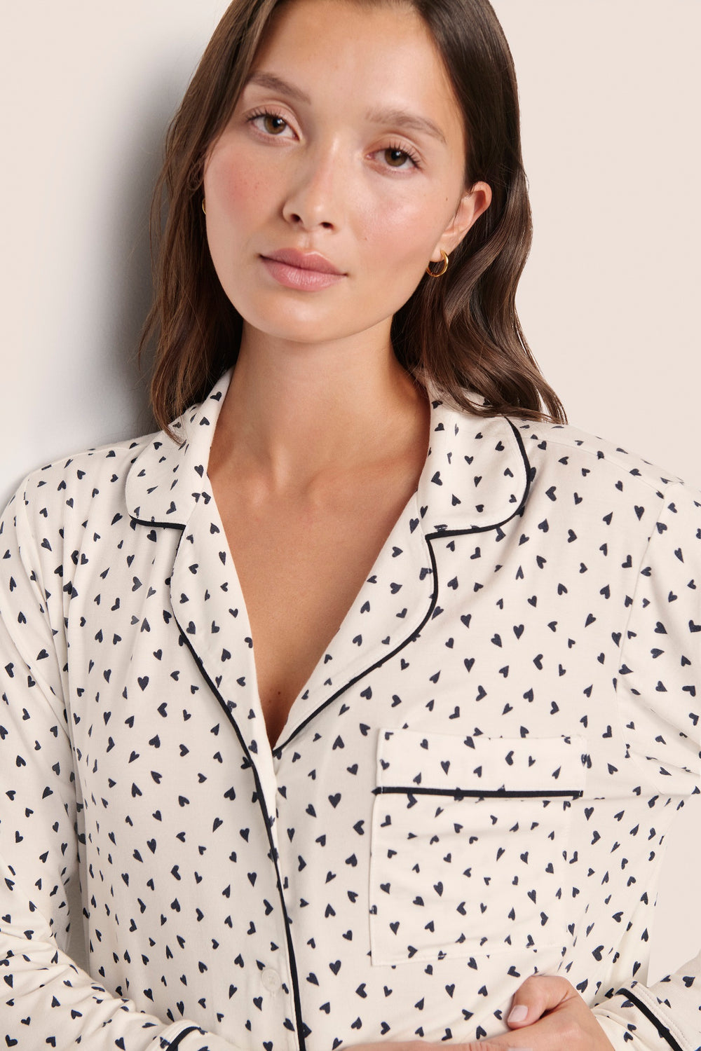 Woman wearing a white pajama top with black heart pattern and piping.