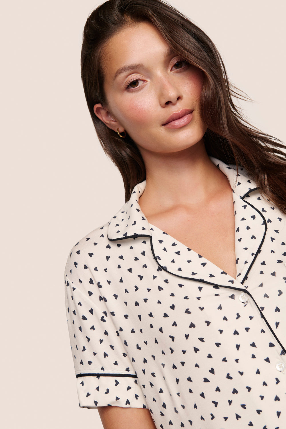 Woman wearing a white pajama top with black heart patterns on a beige background