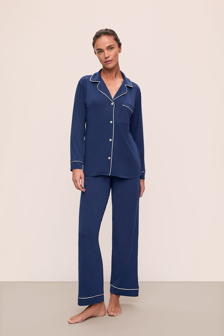 Woman wearing a blue pajama set with white piping on a beige background