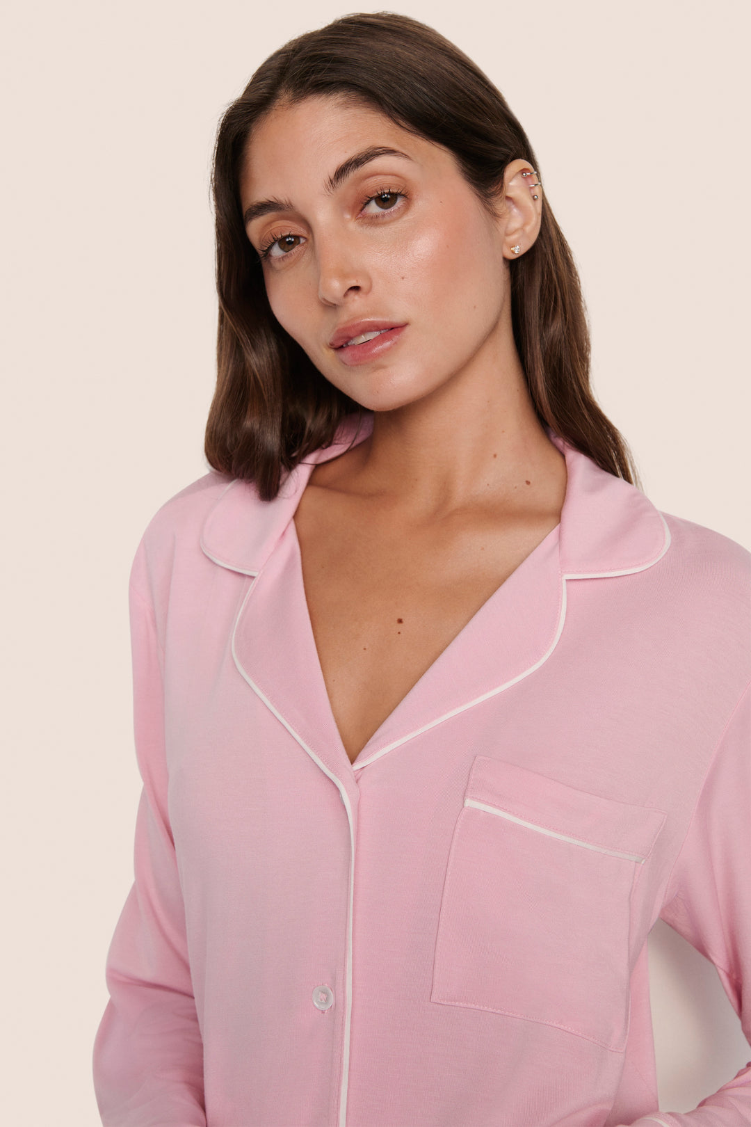 Woman wearing a pink pajama top with white trim on a light pink background