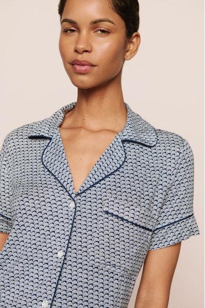 Woman wearing a blue seashell patterned pajama set against a beige background. Cute spring printtern great for vacations and hot sleepers.
