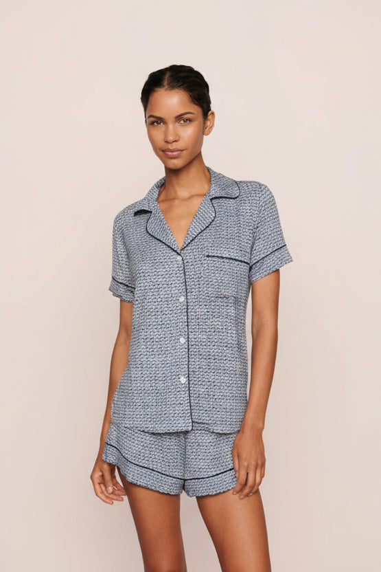 Woman wearing a blue seashell patterned pajama set against a beige background. Cute spring printtern great for vacations and hot sleepers.