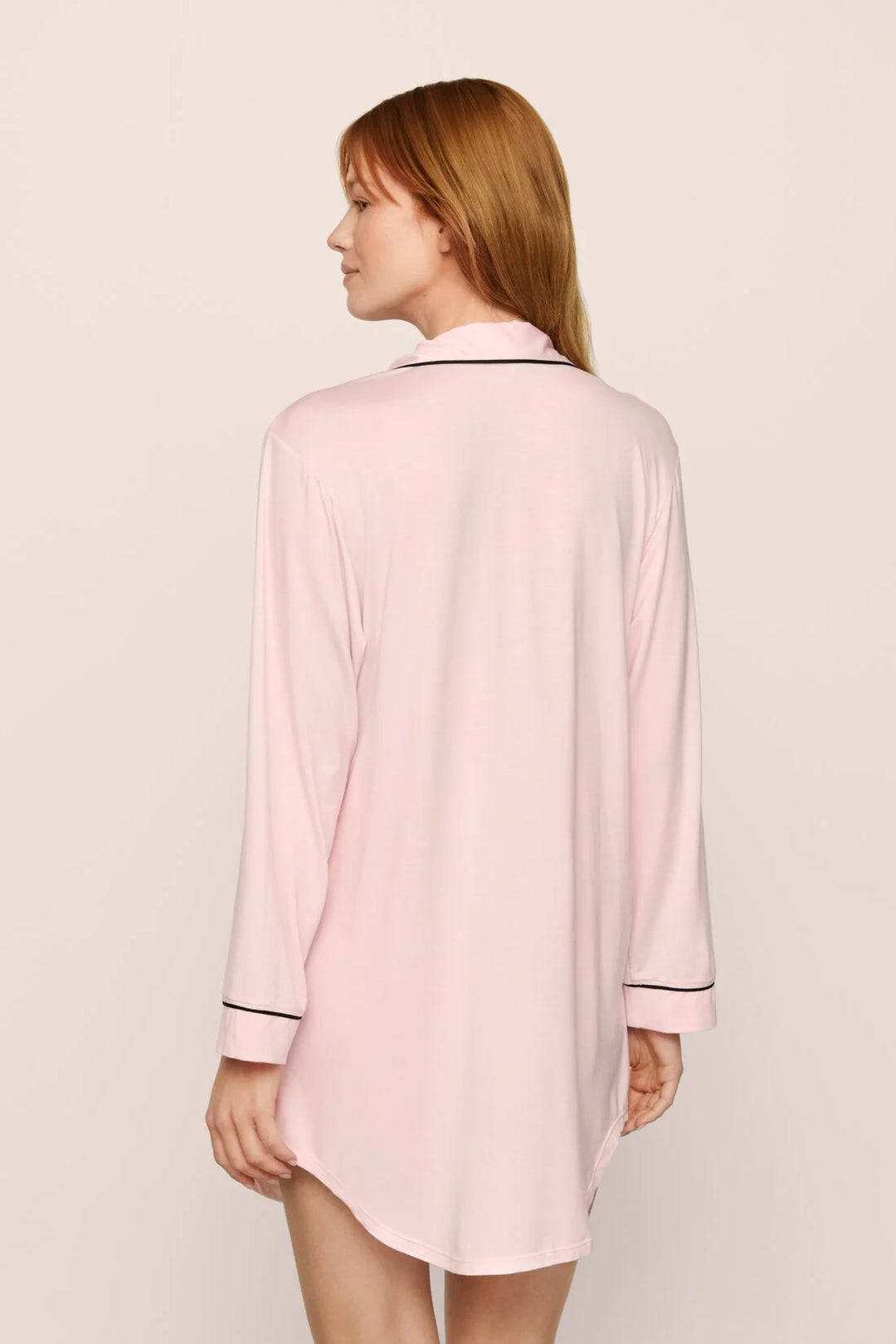 Woman wearing a pink nightshirt with black trim on a beige background