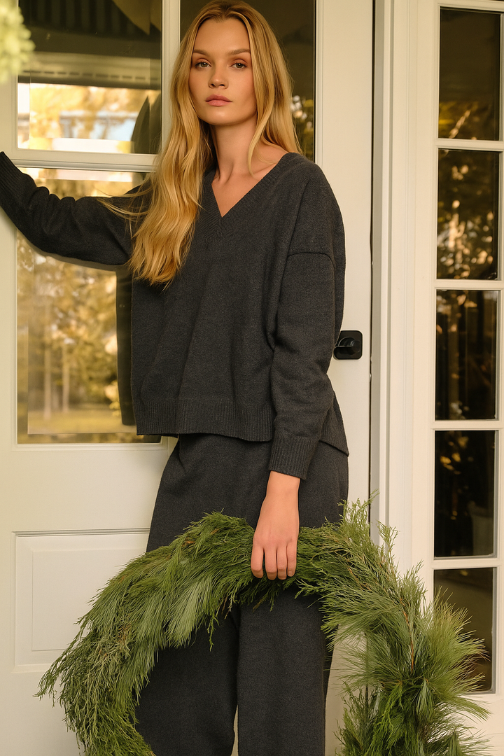 Woman in grey lounge set holding a green wreath in front of a white door