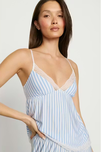 Woman wearing a light blue and white striped dress with lace trim on a plain background