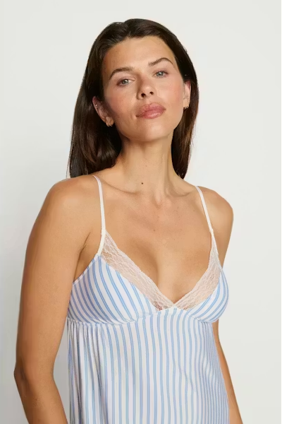 Woman wearing a light blue and white striped nightgown against a plain background