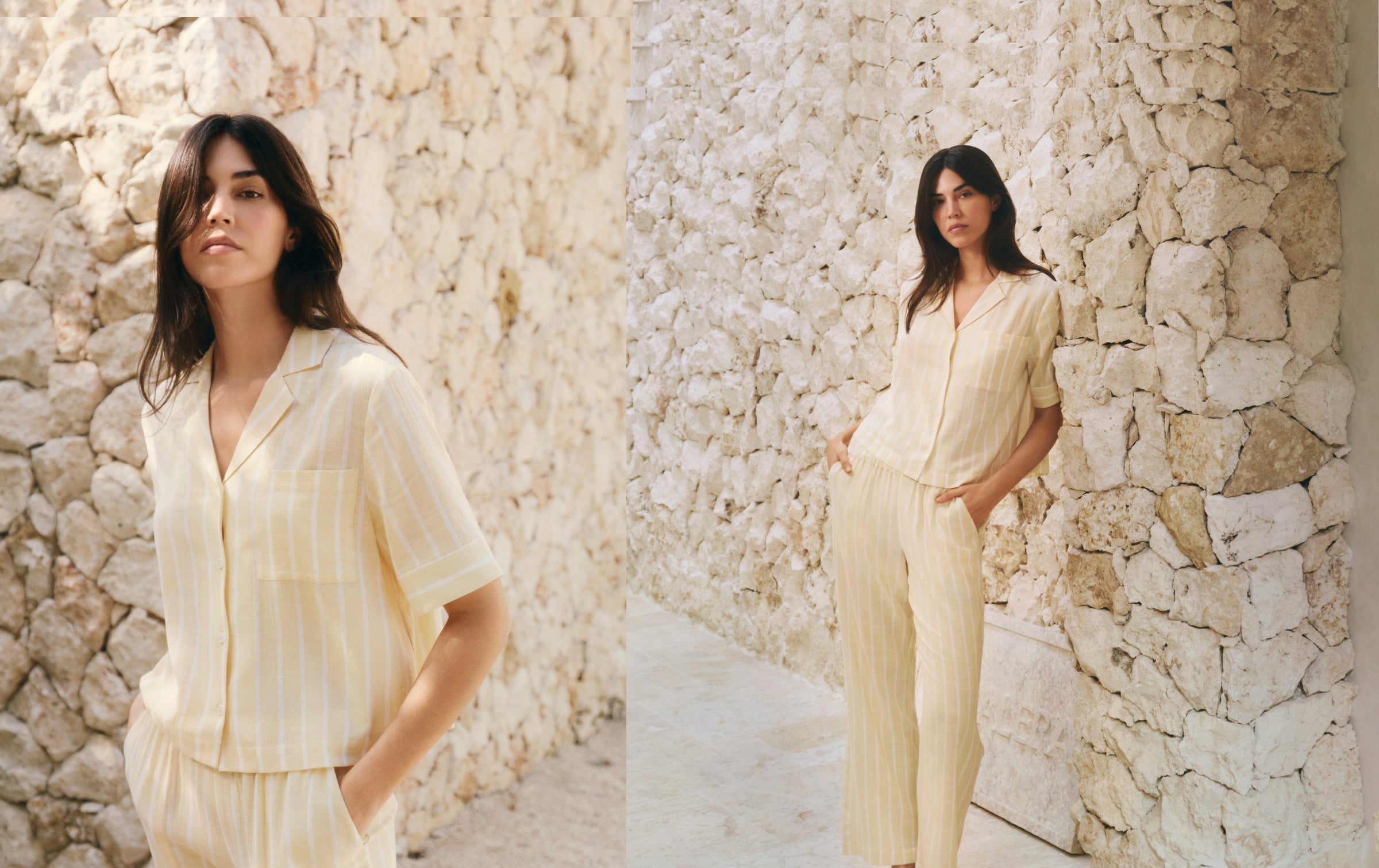 Woman in a light-colored outfit standing against a stone wall.
