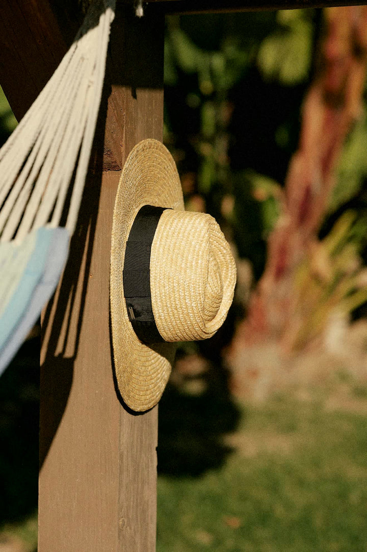 Straw hat with a black band hanging on a wooden post with a blurred natural background