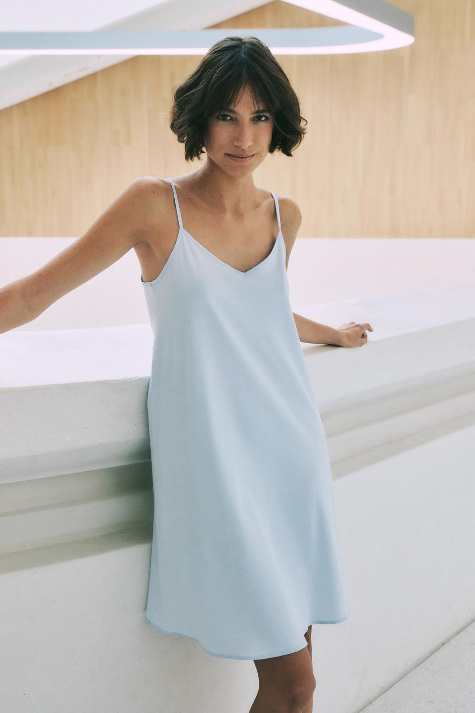 Woman wearing a light blue chemise nightgown in a minimalistic setting