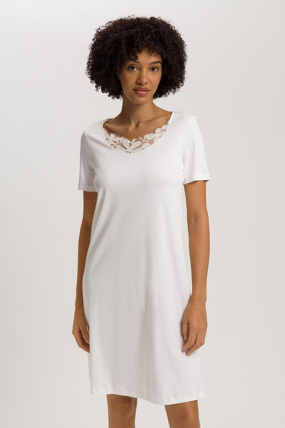 Woman wearing a white nightdress with lace details on a plain background