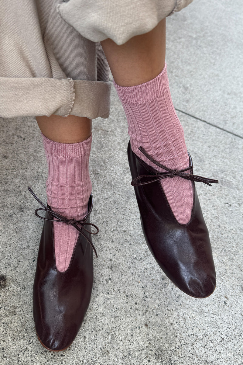 Person wearing pink socks and black shoes on a concrete surface