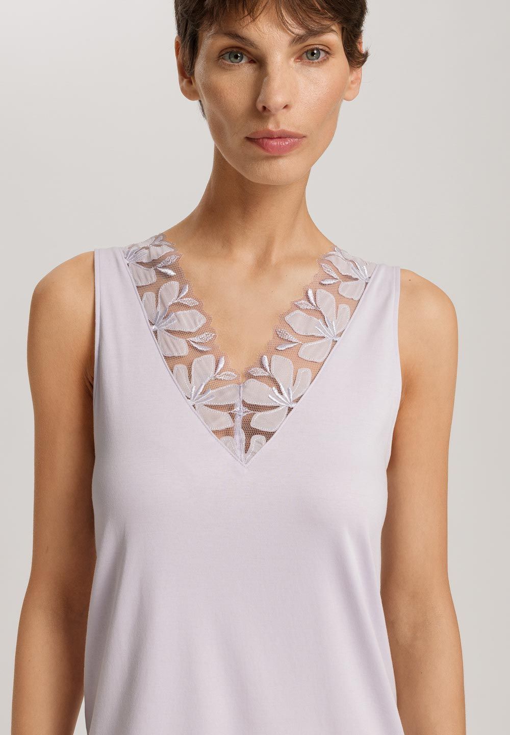 Woman wearing a light purple sleeveless nightgown with floral lace details on a plain background