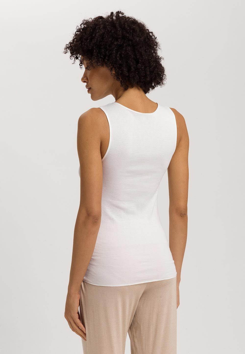 Woman wearing a white sleeveless top against a plain background