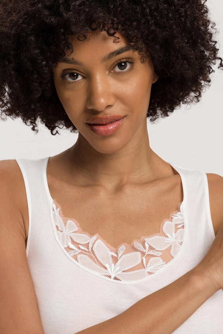 Woman wearing a white tank top with lace details on a plain background
