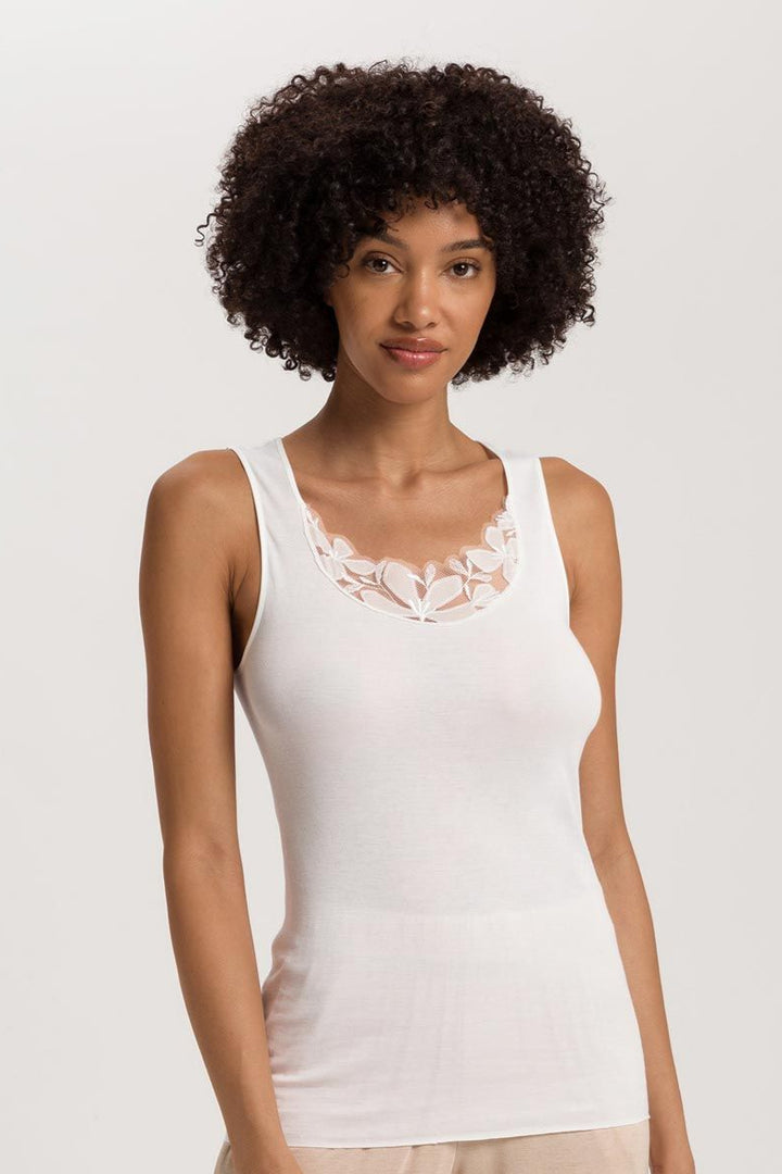 Woman wearing a white tank top with floral embroidery on a plain background