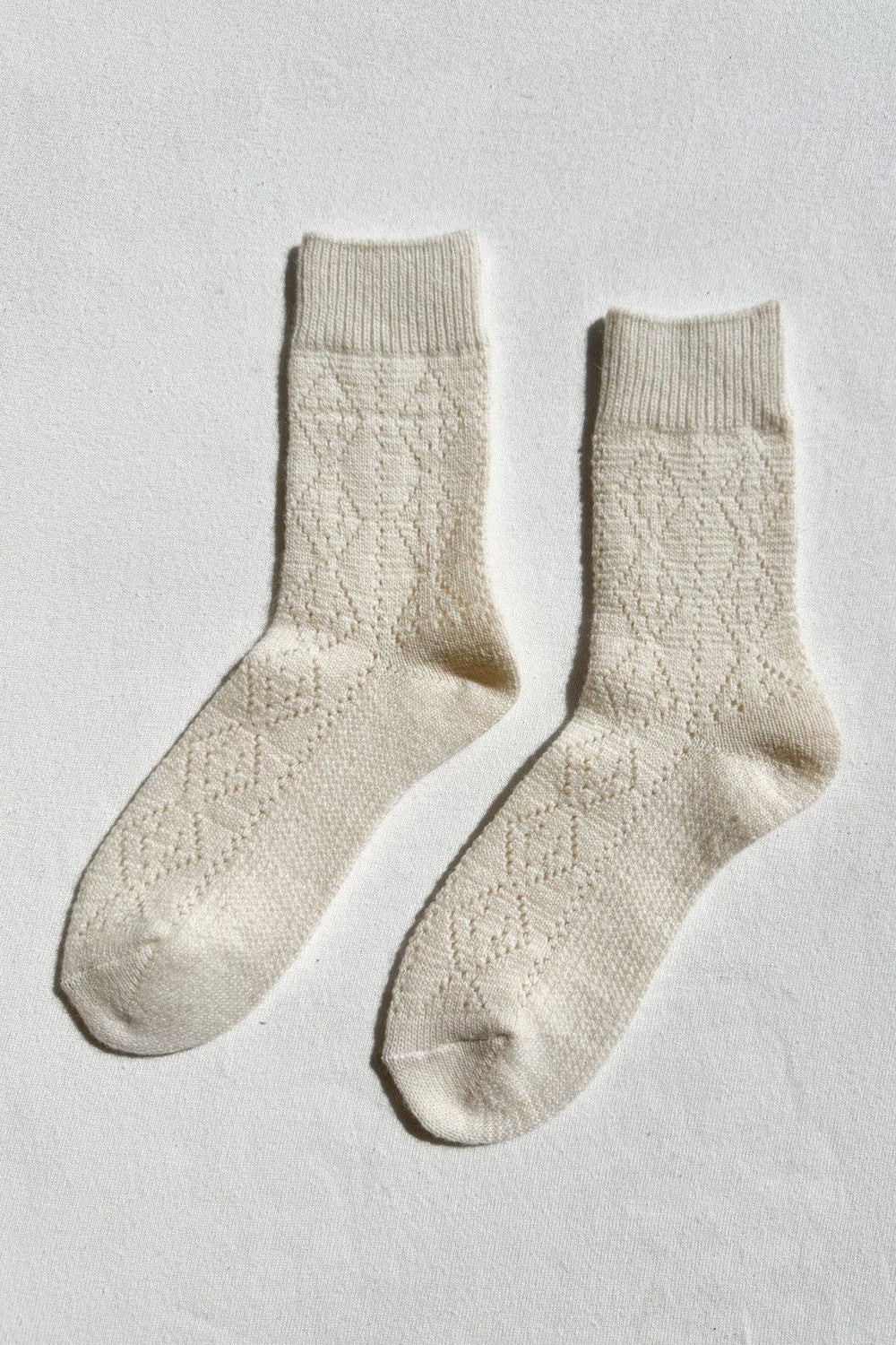 Pair of cream-colored cashmere socks on a light gray background