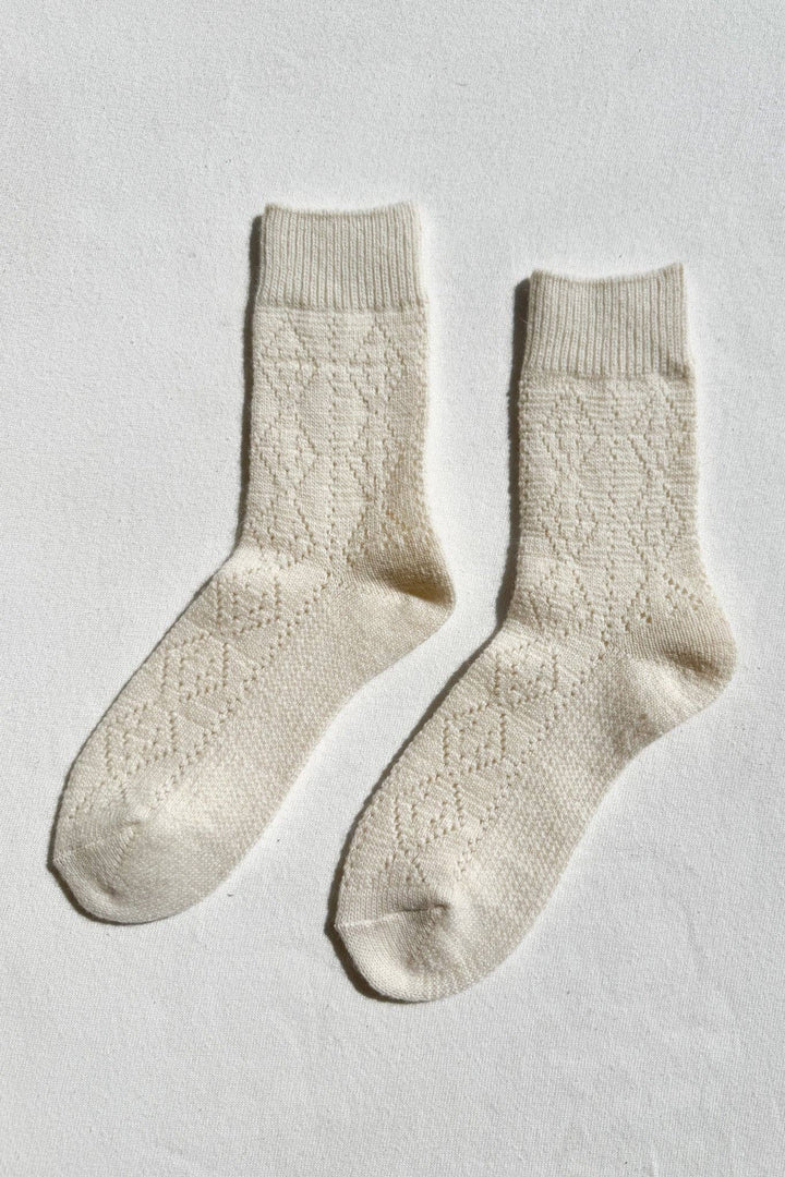 Pair of cream-colored cashmere socks on a light gray background