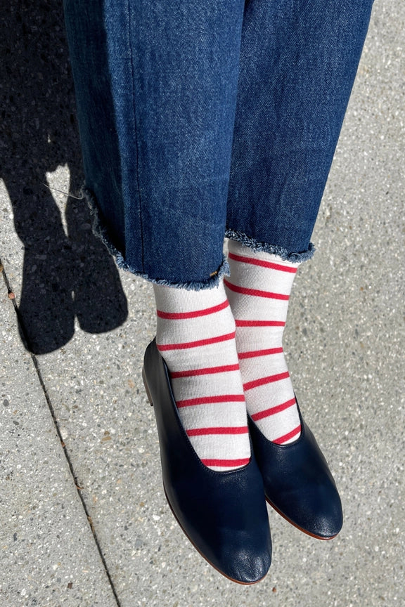 Person wearing blue jeans, red and white striped socks, and black shoes on a concrete surface.
